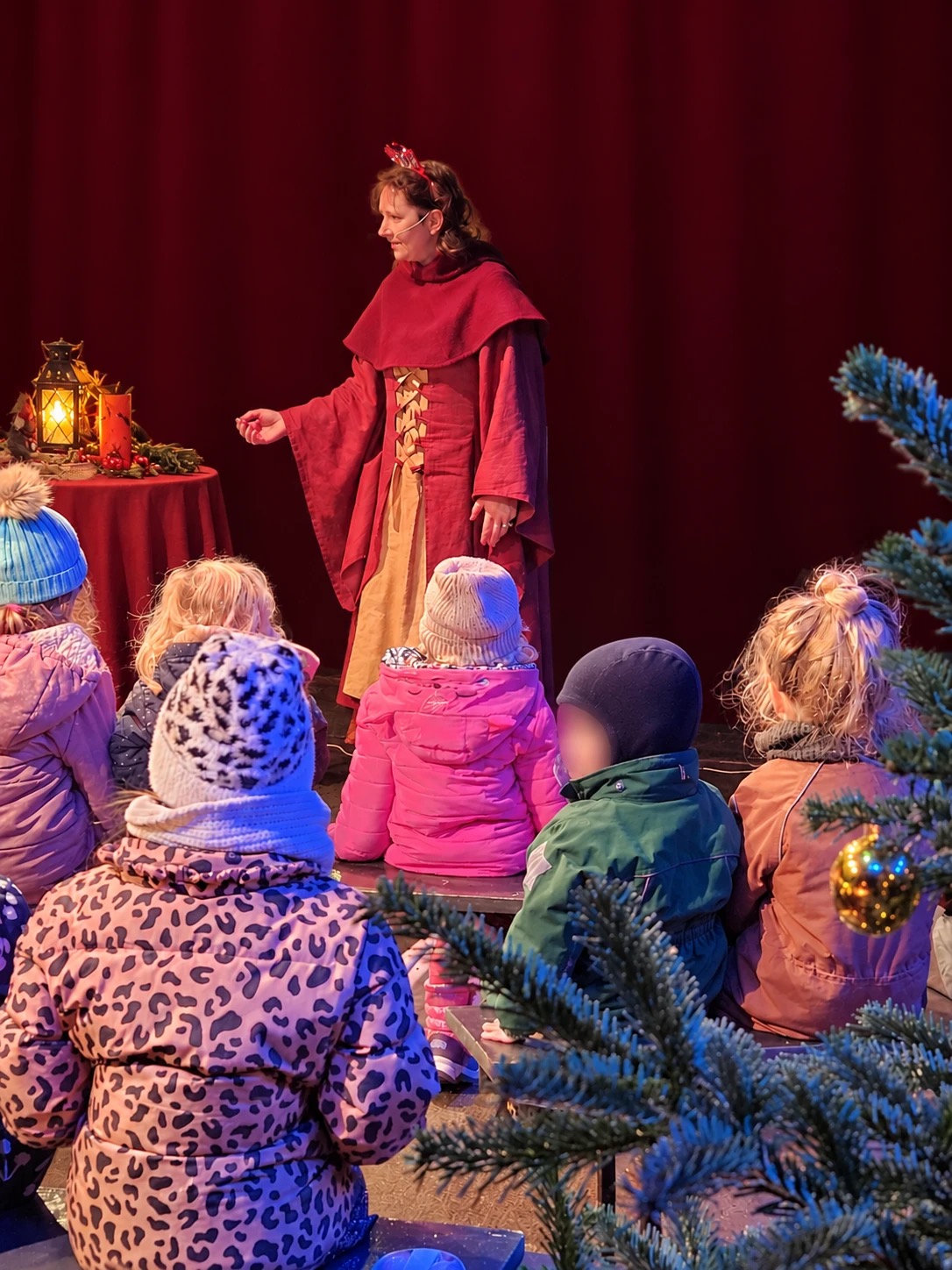 Heike Cordes erzählt auf einer weihnachtlichen Bühne, Kinder in Winterjacken hören zu