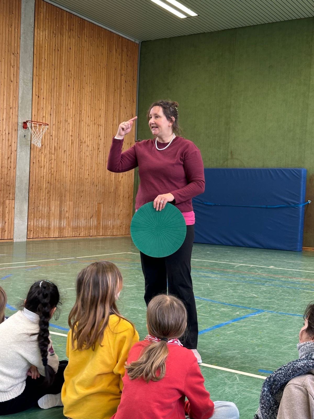 Heike Cordes erklärt einer Gruppe von Kindern in der Turnhalle eine Regel