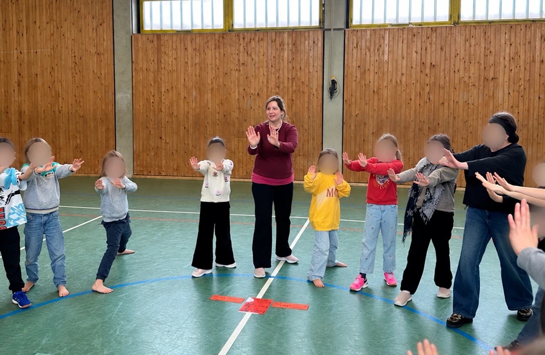 Heike Cordes übt mit einer Grundschulklasse im Kreis eine gemeinsame Geste